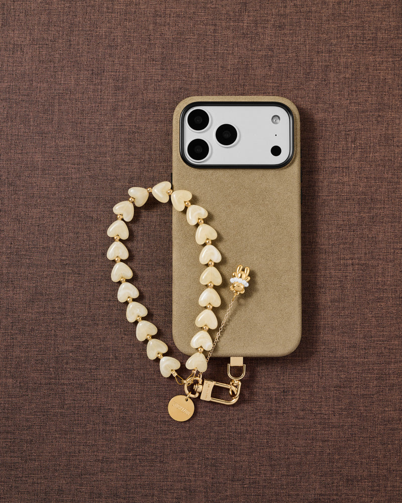Ivory Teddy Heart phone strap and black phone case styled on warm brown fabric — daily wrist carry.
