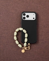 Phone with sage agate stone bead strap on dark brown fabric lifestyle flat-lay