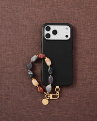 Phone with onyx mix agate stone strap on dark brown fabric lifestyle flat-lay