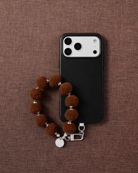 Phone with brown pom-pom strap on styled background by STICKYZOO