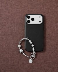 Silver heart-and-star beaded phone wrist strap draped on a black case over mauve linen, with a clear faceted bead, grey faceted star, grey pearl-effect bead and disc