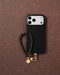 Phone with glossy black bead strap on dark brown fabric lifestyle flat-lay