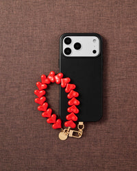 Phone with crimson heart bead strap on dark brown fabric lifestyle flat-lay