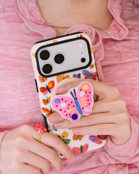 STICKYZOO painted butterfly phone case carried in daily use with fingers gripping the pop-out MagSafe medallion