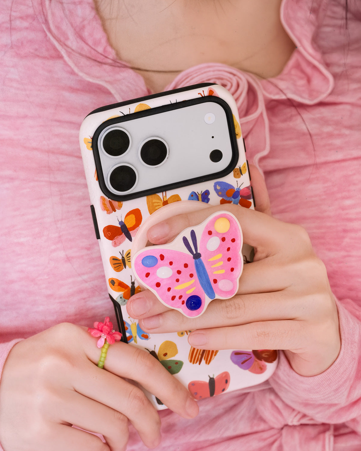 STICKYZOO painted butterfly phone case carried in daily use with fingers gripping the pop-out MagSafe medallion