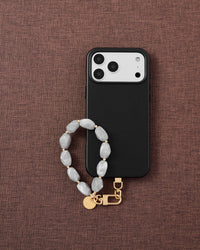 Phone with grey marble stone strap on dark brown fabric lifestyle flat-lay
