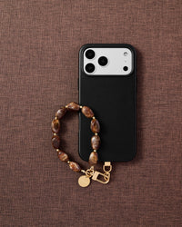 Amber stone phone strap with black phone case on dark fabric lifestyle flat-lay