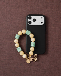 Phone with butter jade orbit strap on dark brown fabric lifestyle flat-lay