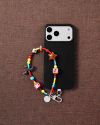 Phone with colorful dachshund charm strap on dark brown textured fabric lifestyle flat-lay