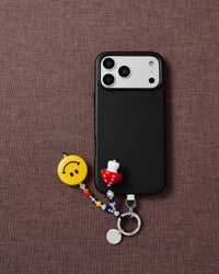 Phone with smiley mushroom charm on brown textile flat-lay showing STICKYZOO phone charm styling