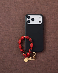 Phone with ruby smoke agate bead strap on dark brown fabric lifestyle flat-lay