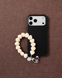 Cream heart bead phone strap styled with phone on brown fabric flat-lay