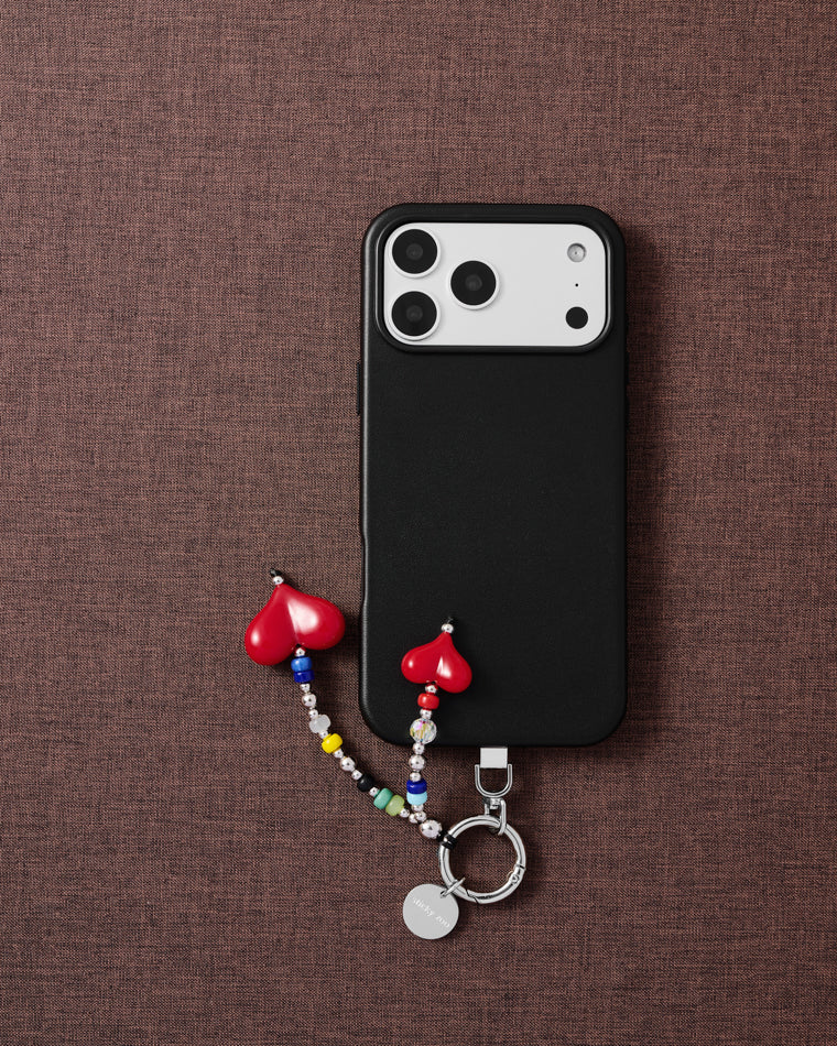 Double red heart phone charm styled with phone on brown fabric flat-lay