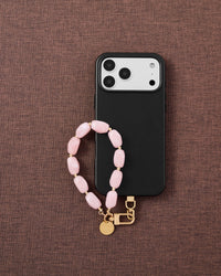 Phone with rose agate stone bead strap on dark brown fabric lifestyle flat-lay