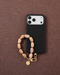 Phone with blush marble stone strap on dark brown fabric lifestyle flat-lay