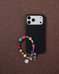 Phone with multicolor heart bead strap on dark brown textured fabric lifestyle flat-lay