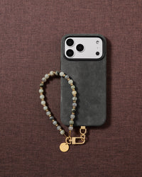 Flat-lay of the handmade grey-green stone wrist strap styled on soft neutral fabric.