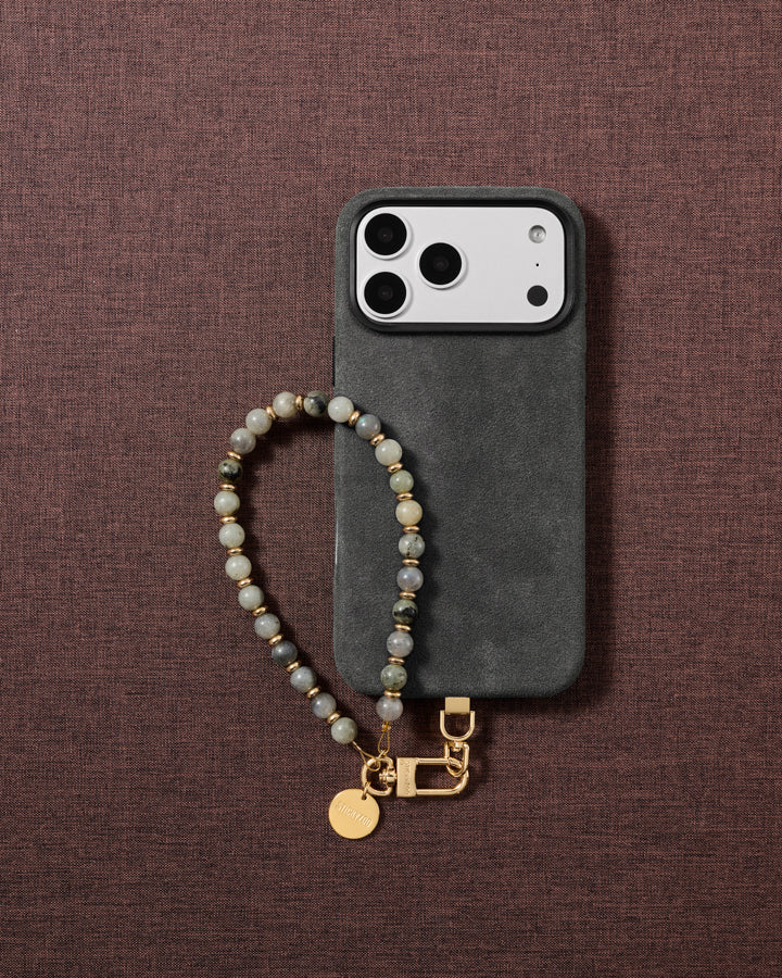 Flat-lay of the handmade grey-green stone wrist strap styled on soft neutral fabric.