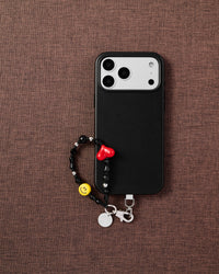 Noir heart smiley phone strap flat-lay on dark brown fabric by STICKYZOO