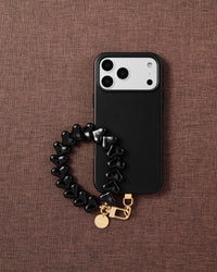 Phone with glossy black heart bead strap on dark brown fabric lifestyle flat-lay