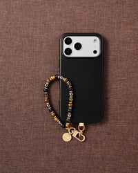 Phone with tiger eye and onyx stone strap on dark brown fabric lifestyle flat-lay