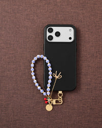 Phone with porcelain cherry charm strap on dark brown fabric lifestyle flat-lay