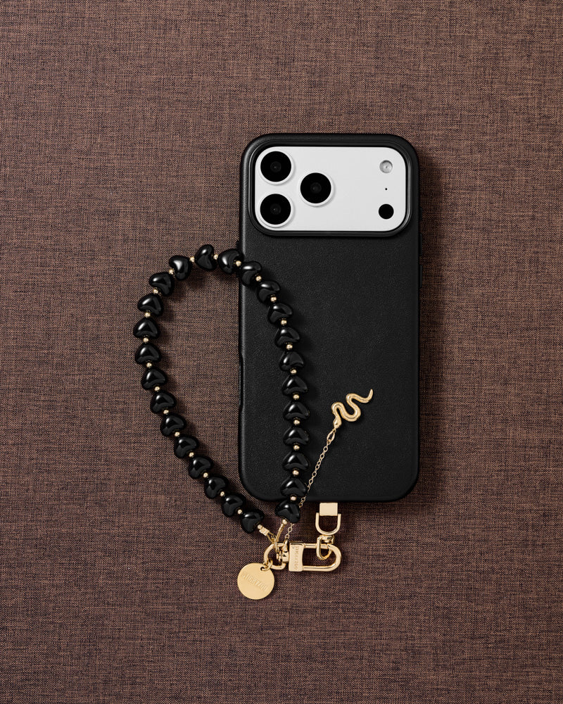 Quiet protective symbol noir snake heart phone strap styled flat-lay with engraved gold snake charm and noir heart beads, designed in Amsterdam