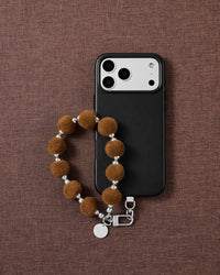 Hazelnut velvet pom phone strap styled on fabric, loved by thousands of STICKYZOO customers