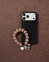 Phone with mocha heart bead strap on dark brown fabric lifestyle flat-lay
