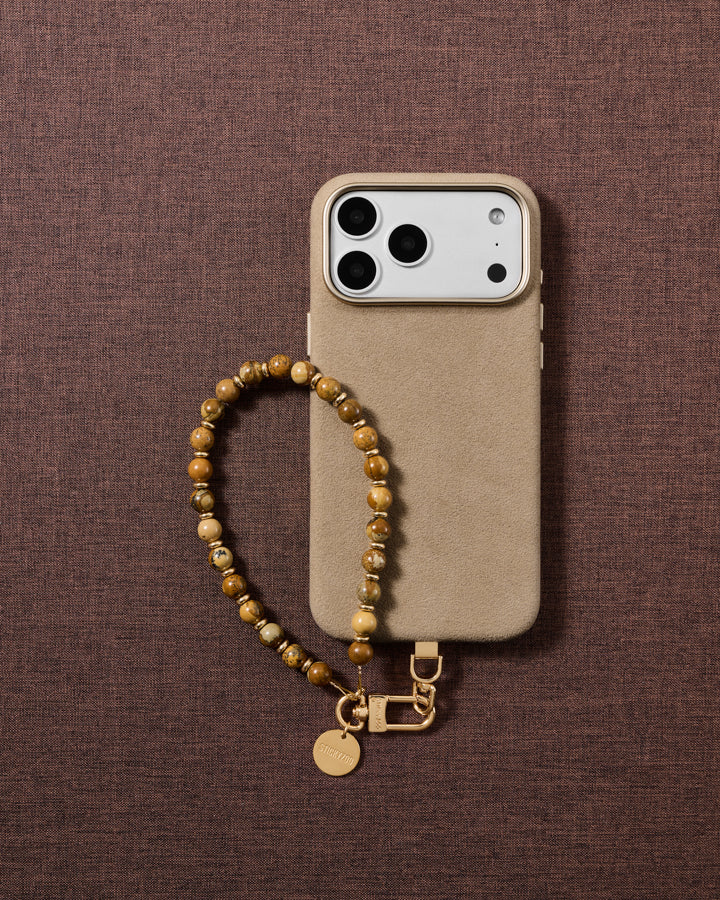 Flat-lay of the handmade tan and brown stone bead phone strap styled on soft neutral fabric.
