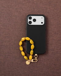 Phone with saffron agate stone bead strap on dark brown fabric lifestyle flat-lay