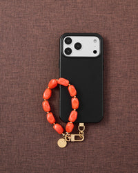 Coral agate stone phone strap with black phone on dark brown fabric lifestyle flat-lay