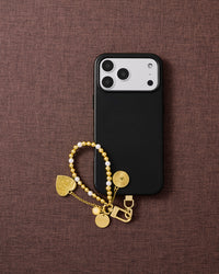 Phone with golden orbit pearl strap on dark brown fabric lifestyle flat-lay