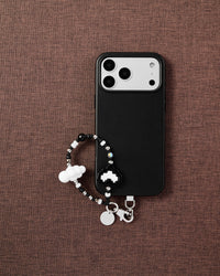 Phone with monochrome pixel heart strap on dark brown textured fabric lifestyle flat-lay