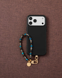 Phone with azure and onyx stone strap on dark brown fabric lifestyle flat-lay
