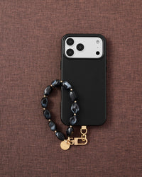 Phone with obsidian agate stone strap on dark brown fabric lifestyle flat-lay