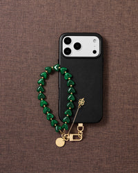 DESIGNED IN AMSTERDAM — Emerald clover heart phone strap styled flat-lay with gold four-leaf clover charm and emerald beads — Rated 4.9 stars