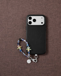 Aurora Starfish beaded wrist strap beside a black phone case on brown fabric, with jelly starfish, blue faceted beads and a silver clasp