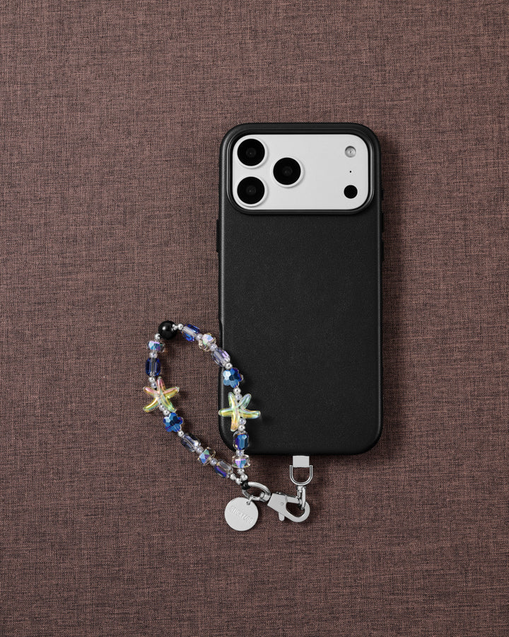 Aurora Starfish beaded wrist strap beside a black phone case on brown fabric, with jelly starfish, blue faceted beads and a silver clasp