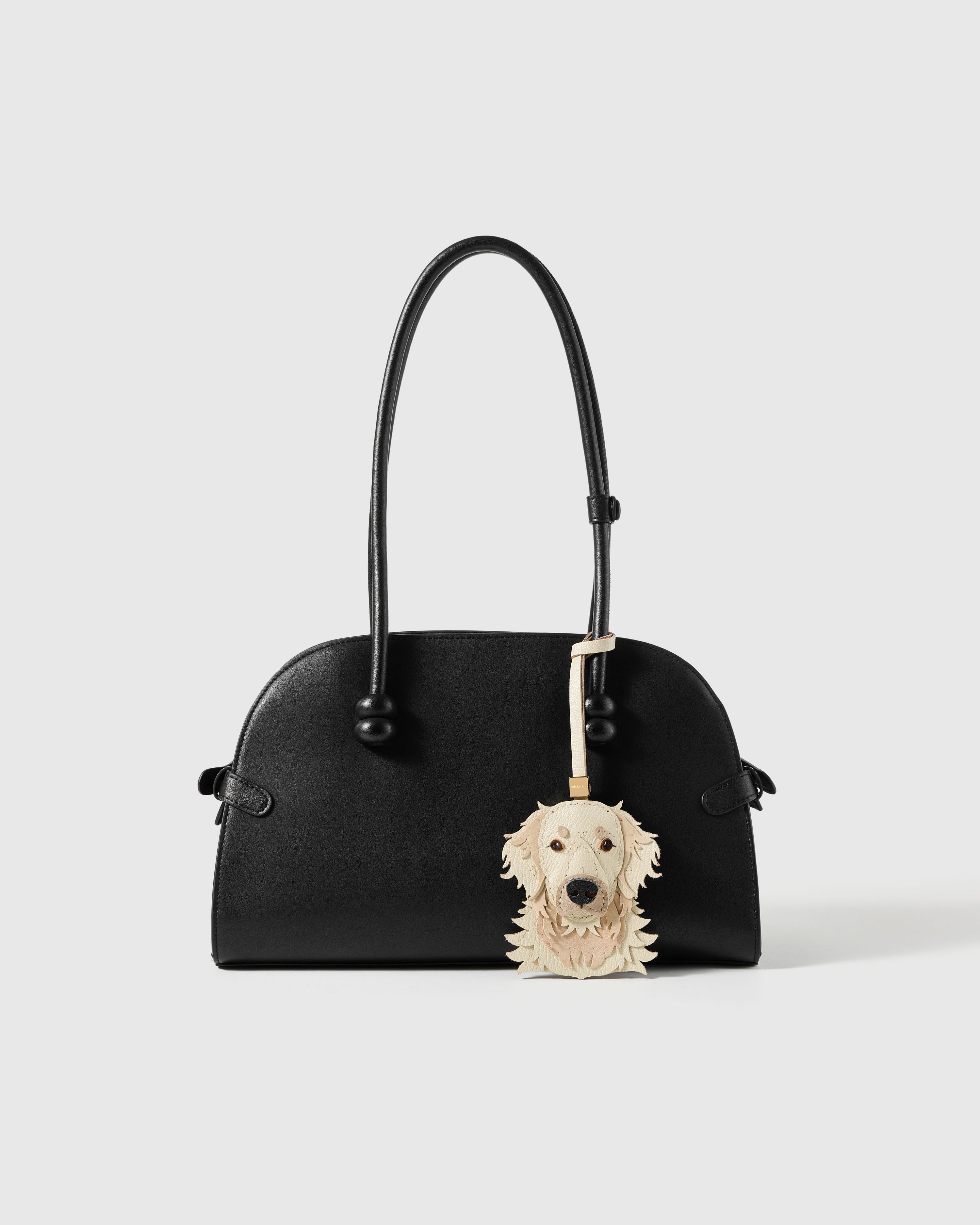 {{Loved by thousands.}} Golden Retriever charm styled on a black handbag — loved by thousands of Golden Retriever people. French Alran goatskin + alcantara suede, 72 hours by hand.