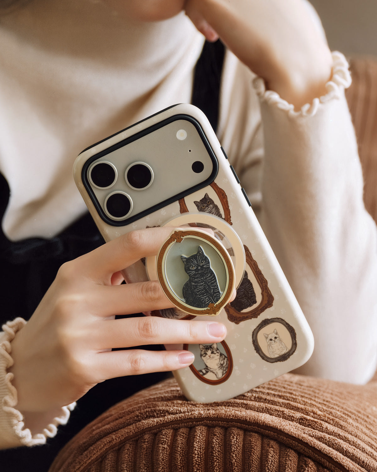 Phone held with fingers around the popped-out MagSafe grip showing the framed tabby on the back of the STICKYZOO case