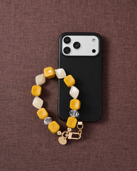 Saffron yellow phone strap with black case on dark fabric styled flat-lay