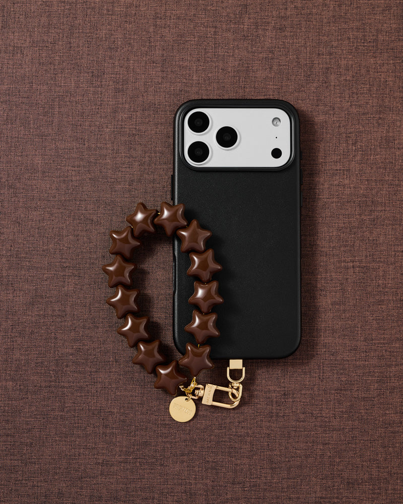 Designed in Amsterdam — cocoa star phone strap and black phone case on a deep cocoa fabric lifestyle flat-lay
