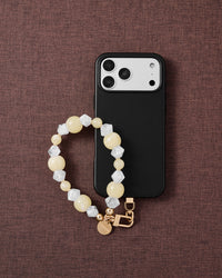 Phone with butter crystal cluster strap on dark brown fabric lifestyle flat-lay