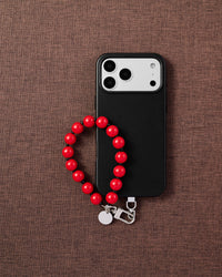 Phone with scarlet red bead strap on dark brown textured fabric lifestyle flat-lay