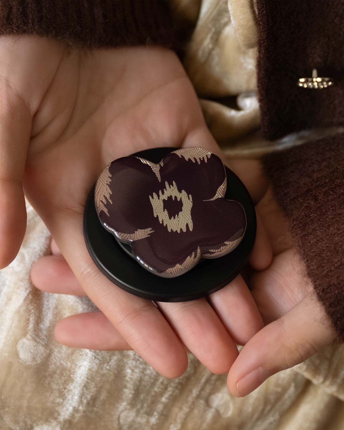 Burgundy poppy MagSafe grip resting in an open palm showing the polycarbonate ring base