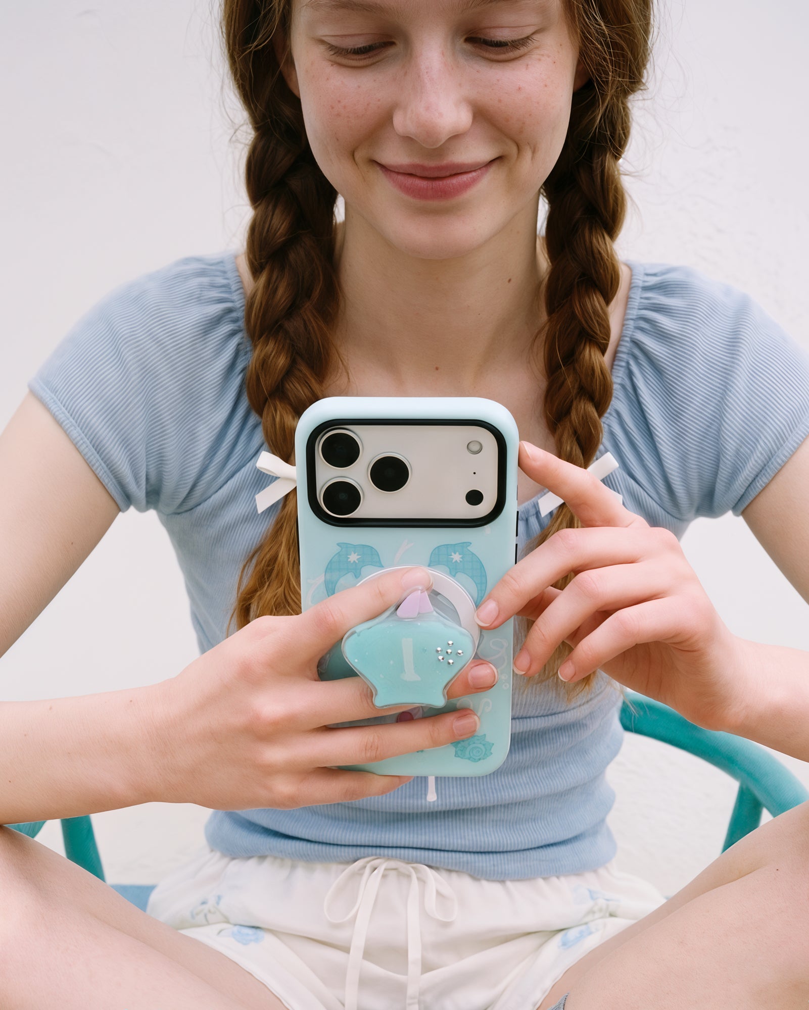 Two-hand hold of the dolphin cove case with the pop-grip extended and the dolphin-heart ocean print in view