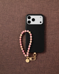 Phone with rose stone strap on dark brown textured fabric lifestyle flat-lay