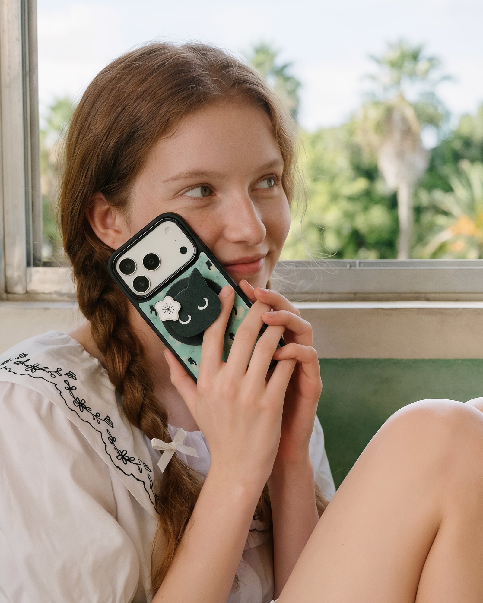 Cat-face pop-grip held one-handed on the back of the midnight cat phone case during a call