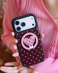 Two hands holding the STICKYZOO starlight heart phone case flat, ring folded against the burgundy shell
